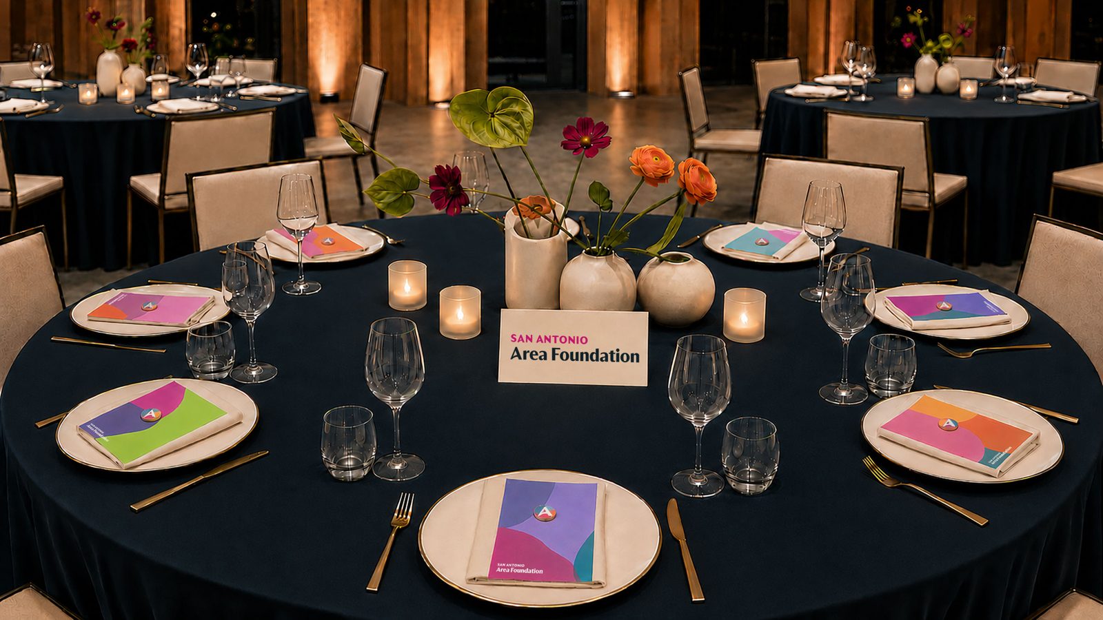 A gala table set in navy linen with cream place cards and mosaic-colored programs